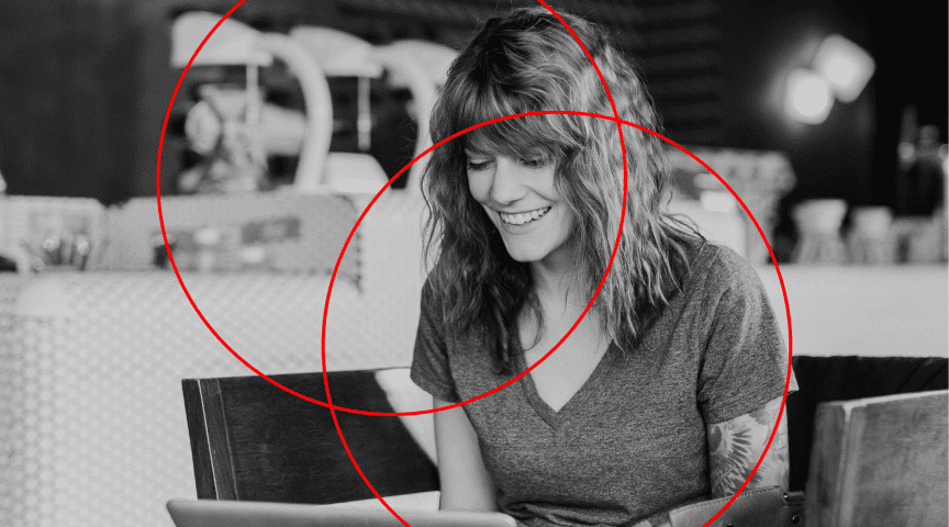 A black and white image of a woman smiling with a computer, with two red circles