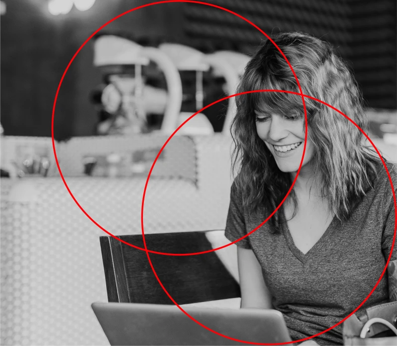 A black and white image of a woman smiling with a computer, with two red circles.