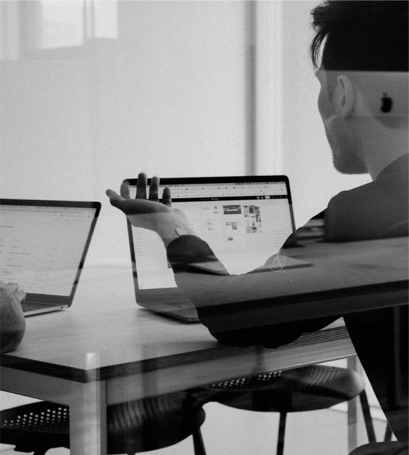 Black and white image of a man with a computer, with another computer screen on the left side.